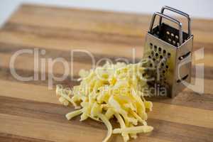 Grated cheese and grater on wooden cutting board