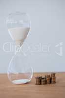 Hourglass and stacks of coins on table