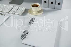 Cup of coffee with spiral notepad on table