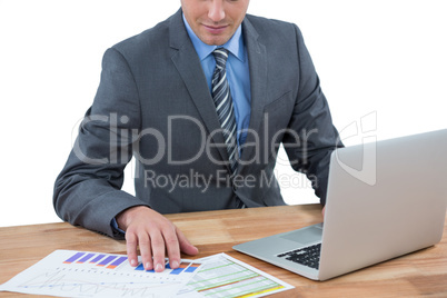 Businessman using laptop while checking graph in office