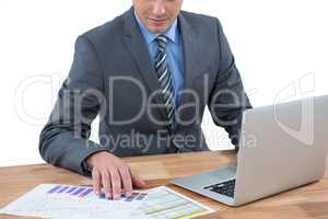 Businessman using laptop while checking graph in office