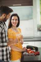 Happy couple toasting glasses of champagne while chopping vegetables in kitchen