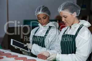 Female butchers maintaining records over digital tablet