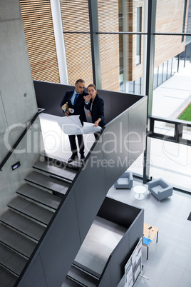 Business colleagues discussing on blueprint while standing on staircase
