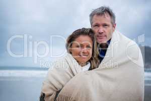 Happy couple wrapped in shawl at beach