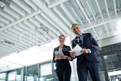 Portrait of business colleagues standing with digital tablet and documents in corridor