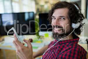 Portrait of smiling business executive listening to music on mobile phone