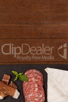 Brie cheese, salami, basil and sliced meat on black serving board