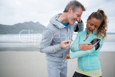 Couple using mobile phone while listening music on beach