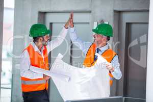Architects holding blueprint while giving high five