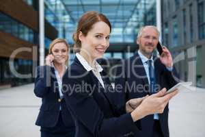 Businesswoman using digital tablet while colleagues talking on mobile phone