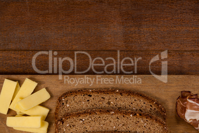 Slices of brown bread, meat and cheese on wooden chopping board