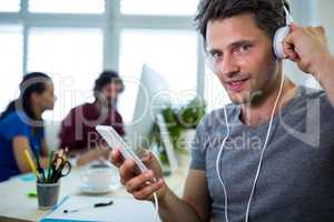 Portrait of smiling business executive listening to music on mobile phone