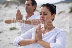 Couple performing yoga on beach