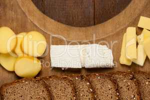 Slices of brown bread and variety of cheese on wooden chopping board
