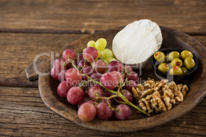 Cheese, grapes, olives and walnut on wooden serving plate