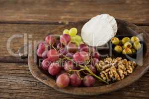 Cheese, grapes, olives and walnut on wooden serving plate