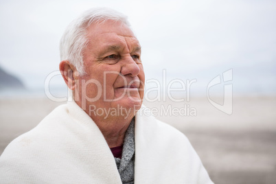 Senior man wrapped in shawl on beach