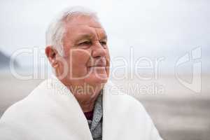 Senior man wrapped in shawl on beach