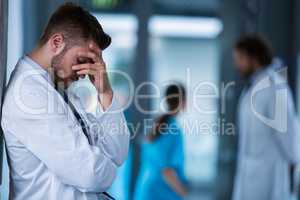 Stressed doctor standing against wall in hospital