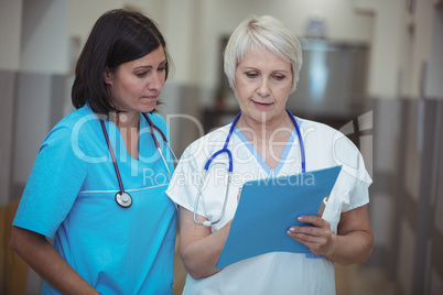Female surgeon and nurse having discussion over file in corridor