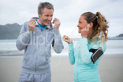 Happy couple listening music on headphones at beach