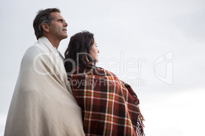 Thoughtful couple wrapped in shawl standing on beach
