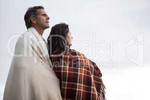 Thoughtful couple wrapped in shawl standing on beach