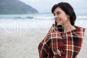 Happy woman wrapped in shawl on beach