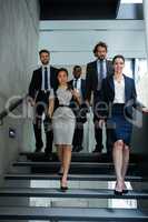 Confident businesswoman with colleagues climbing down the stairs