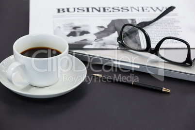 Cup of coffee, spectacles, closed laptop, newspaper and pen