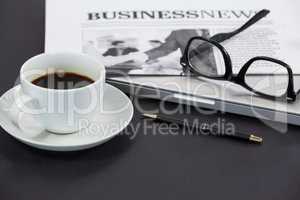 Cup of coffee, spectacles, closed laptop, newspaper and pen