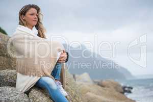 Thoughtful woman wrapped in shawl sitting on rocks