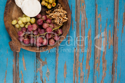 Cheese, grapes, olives and walnuts in wooden bowl