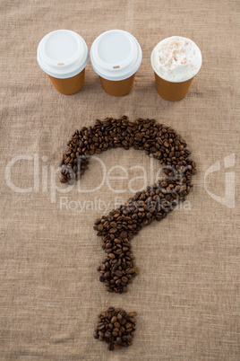 Coffee beans arranged in question mark shape with disposable coffee cups