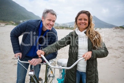 Portrait of couple standing with bicycle on beach