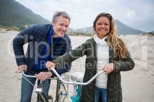 Portrait of couple standing with bicycle on beach