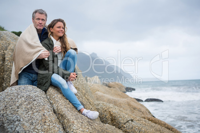 Couple wrapped in shawl sitting on rocks