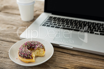 Laptop and doughnut on wooden table