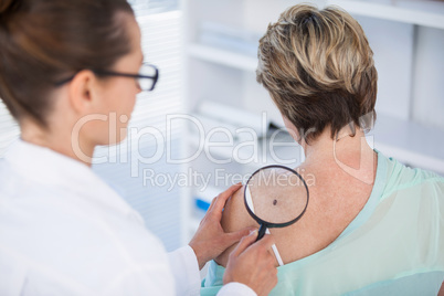 Dermatologist examining mole of female patient with magnifying glass
