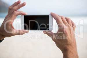 Close-up of mans hand taking picture on mobile phone on beach