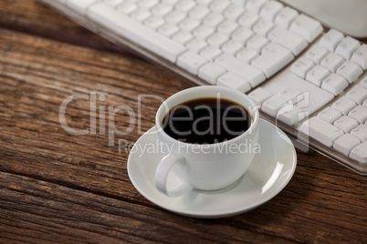 Cup of coffee beside keyboard on wooden table