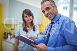 Portrait of doctor interacting and writing on clipboard while consulting patient