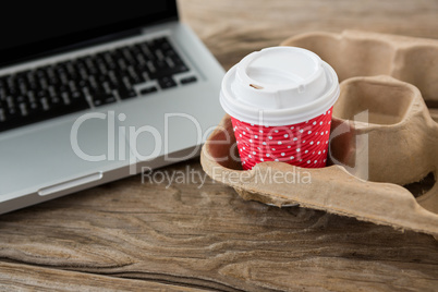 Disposable coffee cup and laptop on wooden table