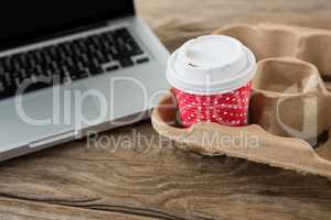 Disposable coffee cup and laptop on wooden table