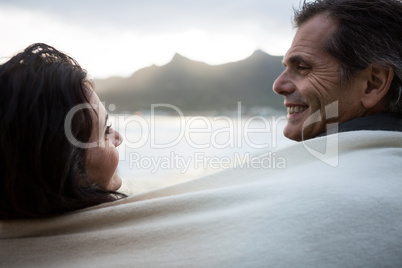 Couple wrapped in shawl looking at each other on beach