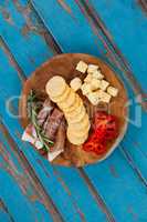 Cheese cubes, capsicum, meat, rosemary and biscuits on wooden board