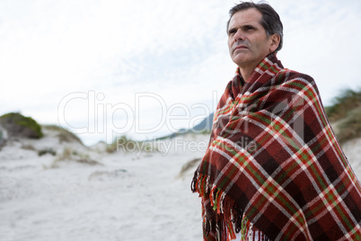 Thoughtful man wrapped in shawl on beach