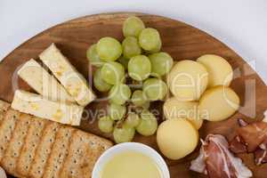Different types of cheese, crispy biscuits, fruits and sauce on wooden board