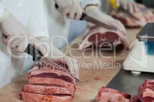 Butcher cutting meat at meat factory